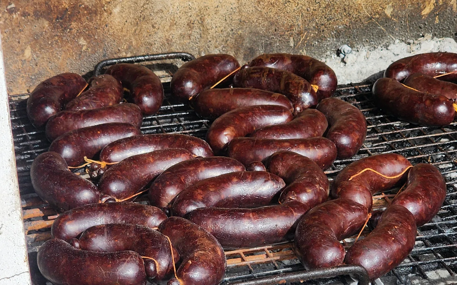Chorizos y morcillas dorándose en fila sobre la parrilla
